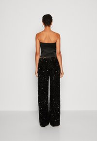 Zwarte satijnen strapless top gecombineerd met hoge taille zwarte, met pailletten versierde, wijde broekspijpen, die een gestructureerde en glanzende afwerking laten zien.