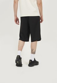 Black athletic shorts with a relaxed fit, made from lightweight fabric, paired with black sneakers and white athletic socks.