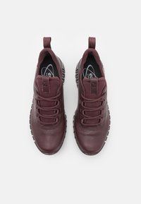 Zapatillas de cuero burdeos con acabado texturizado, cordones elásticos, puntera reforzada y cuello acolchado. Suela de goma con un patrón de banda distintivo.