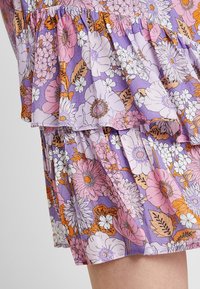 Violetti kukkamekko, jossa on kerroksellisia röyhelöitä, ja se sisältää vaaleanpunaisia, valkoisia ja oransseja kukkia tekstuurilla varustetulla kangastaustalla.