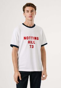 Λευκό βαμβακερό t-shirt με κόκκινο κείμενο "NOTTING HILL 73". Διαθέτει ναυτικό μπλε ριγέ περιλαίμιο και στρώσεις μανικιών. Κλασική εφαρμογή, κοντά μανίκια.