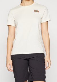 T-shirt in cotone beige con scollo rotondo e maniche corte, con una piccola grafica marrone di un furgone nella zona sinistra del petto.