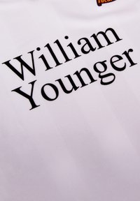 Witte jersey met een gestructureerde afwerking, met "William Younger" in vetgedrukte zwarte letters, prominent gepositioneerd.