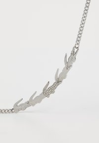 Silver chain necklace featuring multiple crocodile shapes, one adorned with clear rhinestones, creating a textured design.