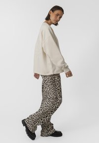 Tejkrém színű, oversize pulóver, amelynek leengedett vállai vannak, és dombornyomott grafika díszíti. Beige leopárdmintás, bő szárú nadrággal és fekete platform cipővel párosítva.