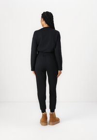 Conjunto de sudadera y joggers negros, con un ajuste relajado, mangas largas y puños en los tobillos. Combinado con botas de tobillo color topo.