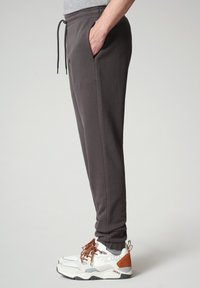 Jogging in cotone grigio scuro con cintura elastica e cordoncino. Le tasche laterali presentano una texture liscia, una vestibilità su misura e una gamba affusolata.