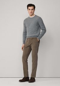 Szary sweter w warkoczowy splot, beżowe spodnie i brązowe sznurowane buty. Sweter ma ściągacze na rękawach i dole; spodnie mają gładką teksturę i dopasowany krój.