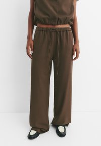 Completo lounge marrone a coste con top corto e pantaloni a gamba larga, dotato di cintura elastica e cordoncino. Scarpe nere e bianche completano il look.