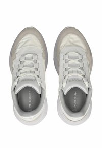 Białe i beżowe trampki o gładkim, matowym wykończeniu, z wyściełanym językiem, siateczkowymi panelami i systemem sznurowania. Logo Lacoste na pięcie.