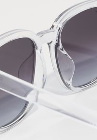 Ochelari de soare din plastic transparent cu lentile gradient întunecate, având o formă îndrăzneață, oversize, în stil cat-eye și o textură netedă.