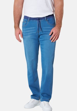 Man wearing light blue relaxed-fit jeans with a dark blue drawstring waist and white sneakers against a plain background.