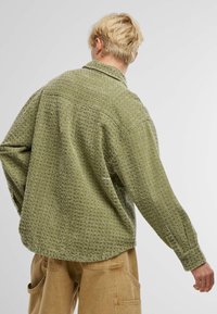 Camisa verde de tejido entrelazado con un patrón texturizado, de mangas largas y cuello con solapa. Presenta un corte relajado y puños abotonados.