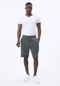Hvid V-hals T-shirt parret med strukturerede grønne shorts og hvide sneakers. Shortsene har en snoretræk i taljen og sidelommer.