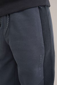 Tumši pelēki treniņbikšu ar strukturētu sānu paneļu, elastīgu vidukļa joslu un auklu. Ar logo uzdruku: "BLUE RIDGE DENIM." Gluda auduma.