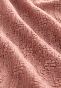 Tessuto strutturato in rosa tenue con motivi in rilievo, caratterizzato da un aspetto morbido e lavorato a maglia. Ideale per coperte o scialli.