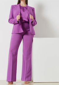 Lila kavaj och matchande vida byxor gjorda av ett mjukt tyg. Kavajen har snedskurna slag och en skräddarsydd passform.