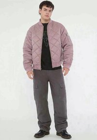 Rožīgs kviltēts bumbers ar ribotām piedurknēm, ar rāvējslēdzēju, kombinēts ar pelēkām kravās biksēm ar sānu kabatām un melniem zābakiem.