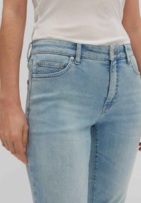 Light blue denim jeans featuring a slim fit, five-pocket design, visible stitching, and metal hardware accents. Smooth texture.