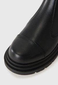 Black leather ankle boot with a rounded toe, featuring a stitched seam and a thick black rubber sole, textured for grip and stability.