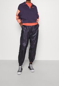 Fialová a korálová mikina na zip s elastickým pasem; černé kalhoty s fialovým zebrovým vzorem; černé vysoké tenisky.