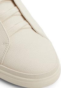 Białe sneakersy z teksturowaną, syntetyczną cholewką, elastycznymi sznurówkami i gładką gumową podeszwą. Okrągły kształt z subtelnymi detalami szwów.