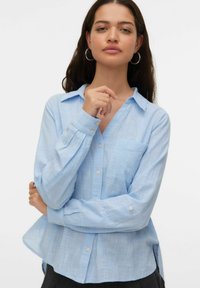 Chemise boutonnée bleu clair en tissu texturé. Dotée d'un col, de manches longues et d'une poche poitrine. Motif à carreaux subtil.