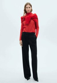Maglia rossa a maniche lunghe in maglia, sovrapposta a un cardigan abbinato, abbinata a pantaloni neri a gamba larga a vita alta. Texture morbide e design aderente.