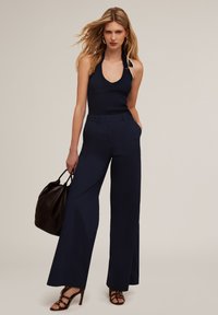 Mörkblå vida byxor i kombination med en svart ribbad halterneck-top. Modellen håller en brun läderväska. Slät tyg med en skräddarsydd passform.