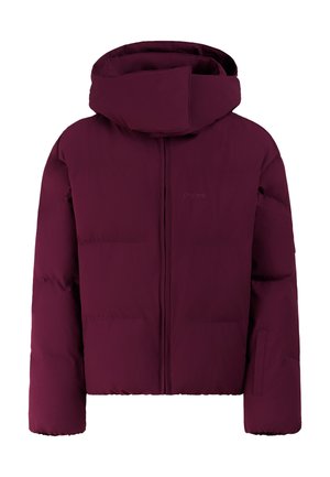 Jeune femme debout en doudoune violette, gants noirs, pantalon noir, bonnet tricoté rayé et lunettes de soleil roses sur un fond uni.