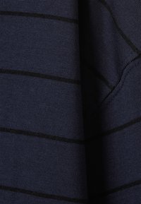 Υφάσμα ναυτικό μπλε με διακριτική υφή που παρουσιάζει οριζόντιες μαύρες ρίγες. Κοντινή λήψη που αναδεικνύει τη δομή του πλεκτού και τις λεπτομέρειες του μοτίβου.