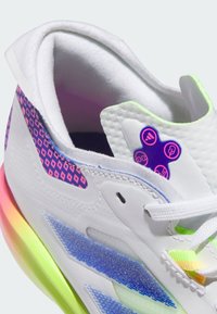 Baskets blanches de sport avec un dessus texturé, des motifs géométriques colorés en rose et bleu, et une semelle dégradée arc-en-ciel.