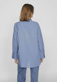 Svijetloplava košulja dugih rukava od glatkog materijala, sa stražnjim jarmom, blago zakrivljenim rubom i dugmadi na manžetama.