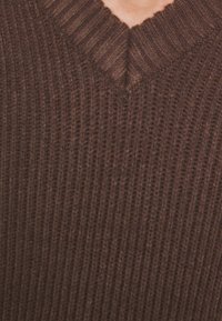 Brązowy sweter z prążkowanego materiału z dekoltem w kształcie litery V. Tkanina jest miękka i lekko elastyczna, z pionowymi żłobieniami na całej powierzchni.