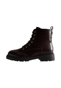 Bottines en cuir marron foncé avec un bout rond, un laçage sur le devant, des œillets dorés, et une semelle en caoutchouc noire. Elles possèdent une languette au talon.