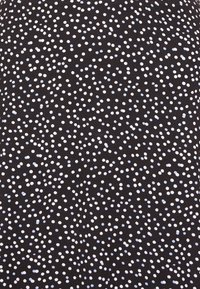 Tissu noir avec un motif de points blancs et bleu clair dispersés, offrant une apparence texturée avec des tailles de points variées.