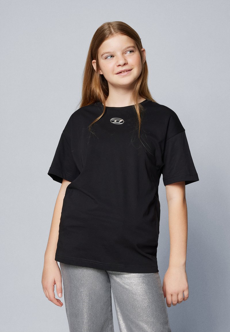 Tricou negru din bumbac, cu guler rotund și mâneci scurte, având un mic logo metalic în centru. Purtați-l cu pantaloni strălucitori argintii.