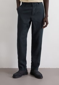 Donkergroene linnen pantalon met een rechte snit, voorzien van zijzakken en een tailleband met een enkele knoop, gecombineerd met zwarte instappers.