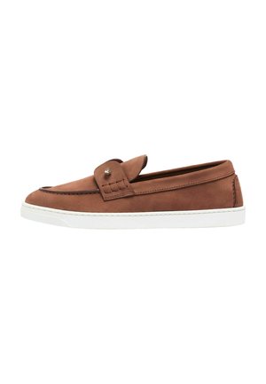 Mocasín marrón de cuero tipo slip-on con suela blanca de goma y un pequeño detalle metálico en la correa superior, mostrado de lado.