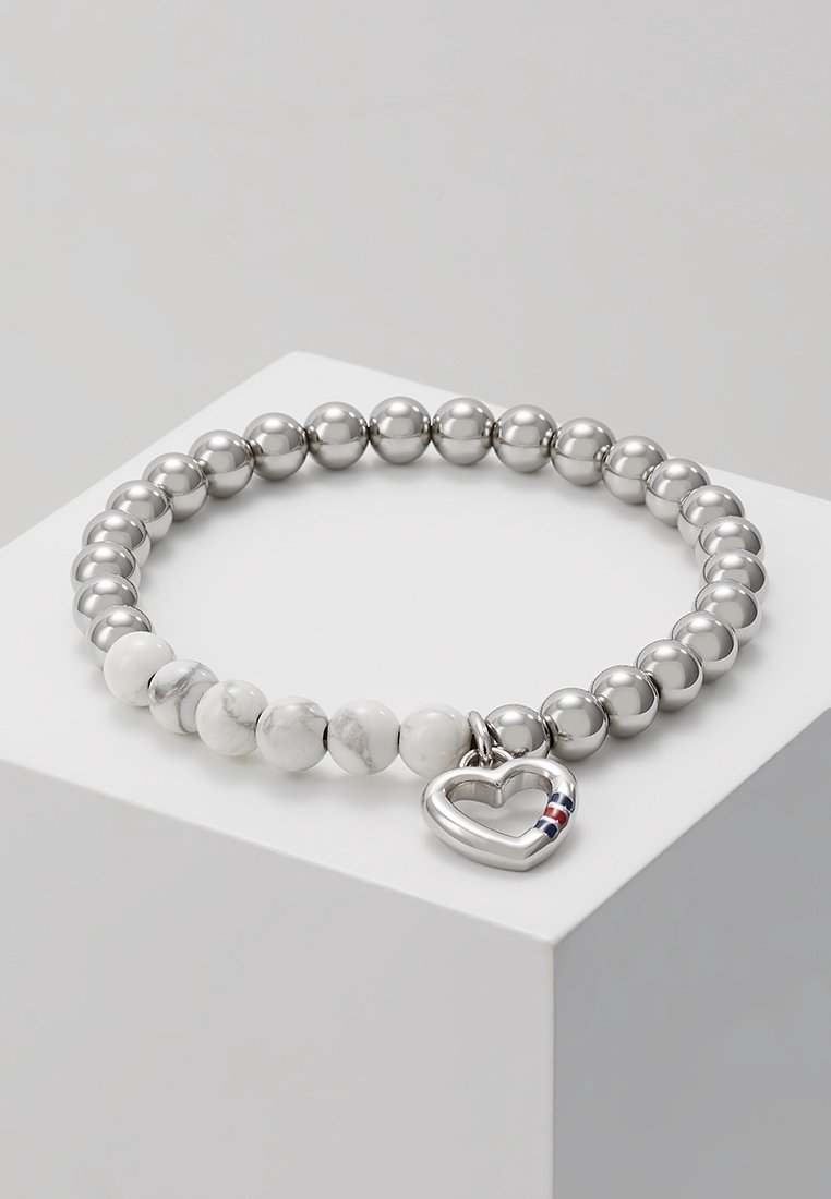 Bracelet de perles avec des perles alternées argentées et marbrées blanches, ornée d'un charme en forme de cœur argenté avec des rayures rouges et bleues.