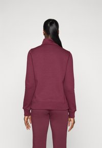 Burgunderfarbener Pullover mit hohem Kragen, gerippten Bündchen und Saum, kombiniert mit passenden Hosen. Glatte Textur, taillierter Schnitt.
