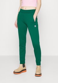 Zelené bavlněné tepláky s tapered střihem, elastickým pasem, bočními kapsami a bílým logem Adidas. Spárovány s béžovými kotníkovými botami.