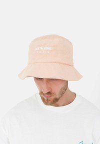 Perzikkleurige bucket hat van terrycloth met gestikt logo "SIXTH JUNE PARIS" op de voorkant. Brede rand en zachte textuur.