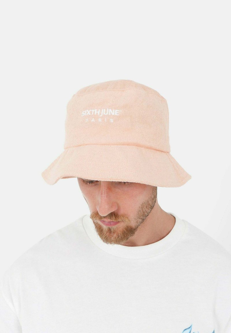 Perzikkleurige bucket hat van terrycloth met gestikt logo "SIXTH JUNE PARIS" op de voorkant. Brede rand en zachte textuur.