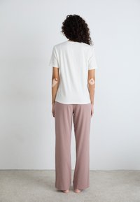 T-shirt blanc à coupe décontractée et pantalon rose poudré ample. Texture de tissu douce, design simple sans motifs ni accents visibles.