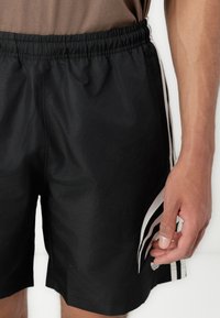 Sorte atletiske shorts med elastisk talje, med hvide sidekanter og et glat, let materiale.