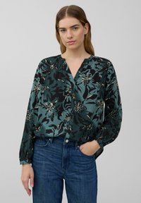 Blumenbluse in grün, schwarz und creme mit entspannter Passform, V-Ausschnitt und langen Ärmeln. Glattes Material mit einem auffälligen Blumenmuster.