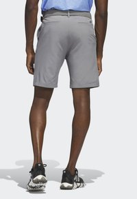 Pantaloni corti grigi con una texture liscia, dotati di due tasche posteriori e una cintura intrecciata. Sneakers bianche e nere con una suola decorata.