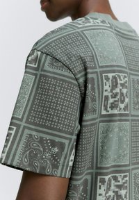 Kortærmet skjorte i et afdæmpet grønt stof med et blandet mønster af firkanter, paisley-designs og geometriske former.
