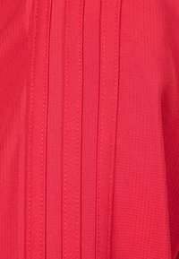 Roter Stoff mit einem strukturierten Muster, das vertikale Falten und kontrastierende Nähte aufweist. Glatte Oberfläche mit einem leichten Glanz.